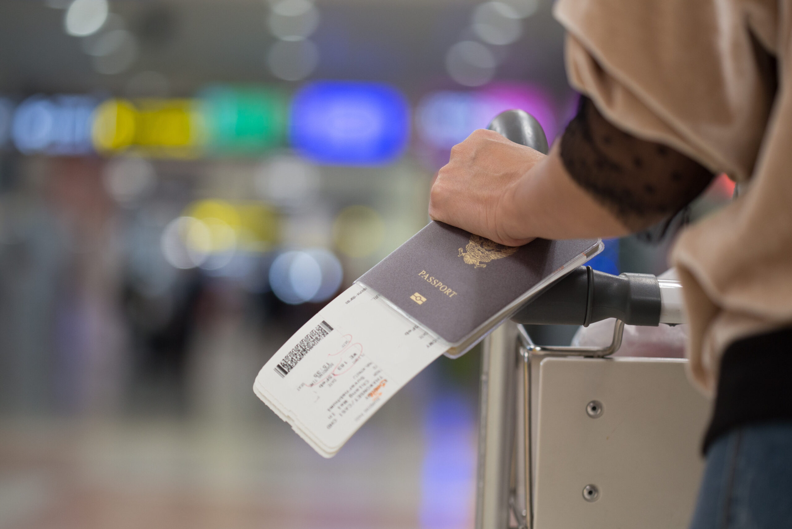Close up of person holding a passport and boarding passes while pushing luggage through an airport