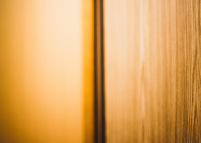 Warm toned image of a hotel room door with peephole in an orange hallway