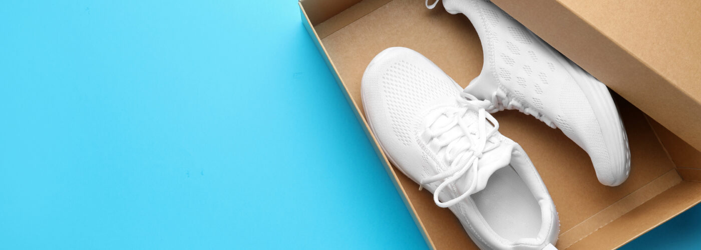 New white shoes inside brown shoe box on a bright blue background