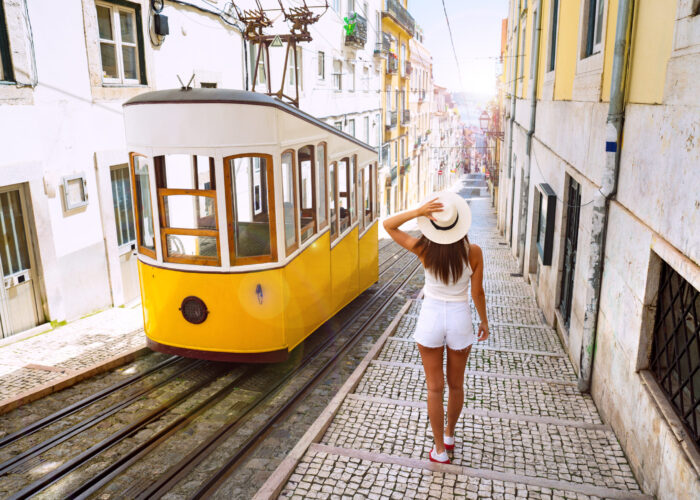 Woman wearing summer clothes, walking down a street in Lisbon, Portugal past a tram