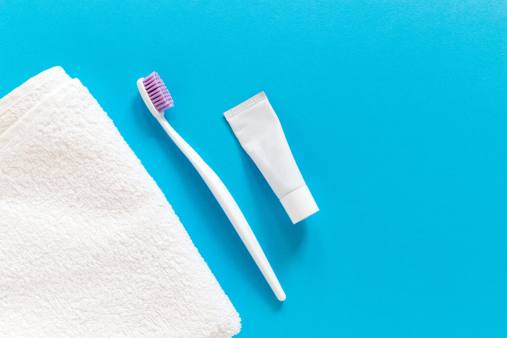 Flat lay of a toothbrush, toothpaste, and white towel on a bright blue background