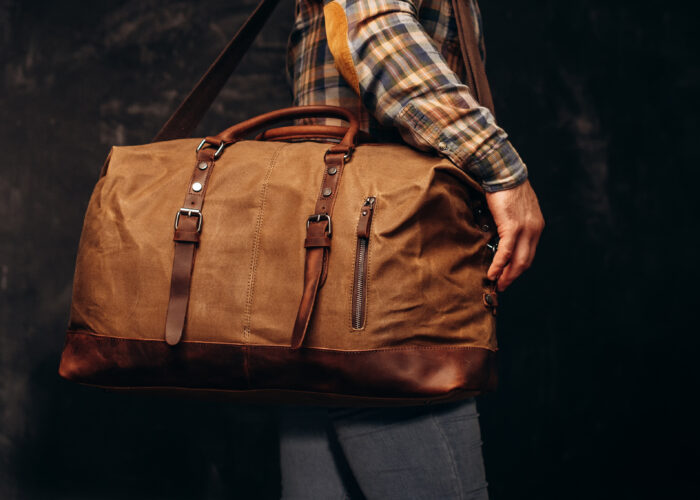Close up of man holding a brown leather duffel bag