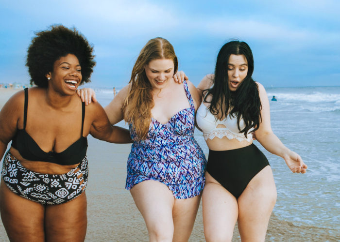 Three women walking through waves at the beach and laughing